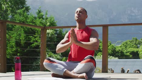 relaxed biracial man sitting on terrace and meditating