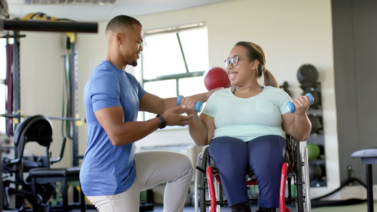 Assisting woman with paraplegia in wheelchair, therapist guiding exercise with dumbbells in rehab