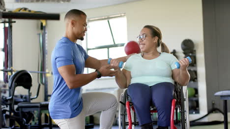 assisting woman with paraplegia in wheelchair, therapist guiding exercise with dumbbells in rehab