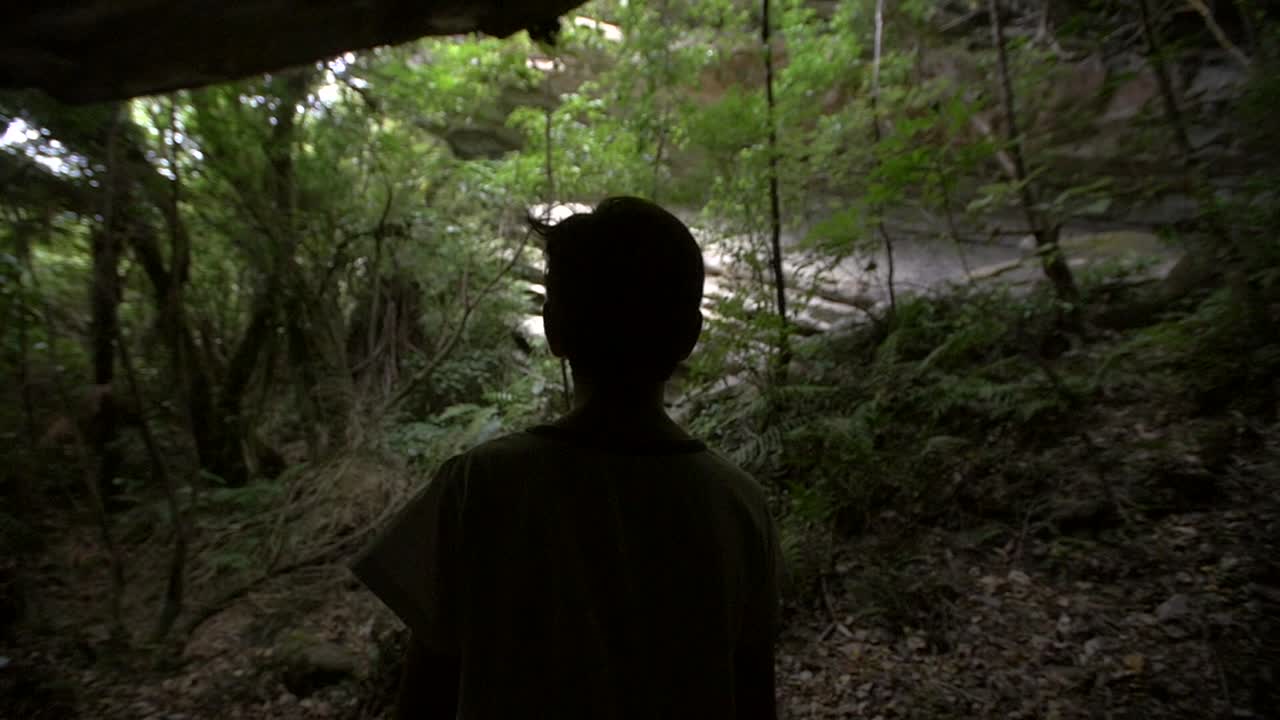 동굴 밖을 내다보는 실루엣 어린 소년