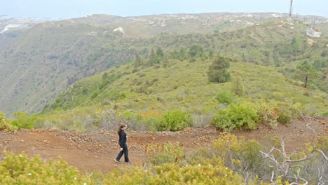 Girl-walking-down-dirt-path,-view-over-coast-and-green-hills-of-Tenerife