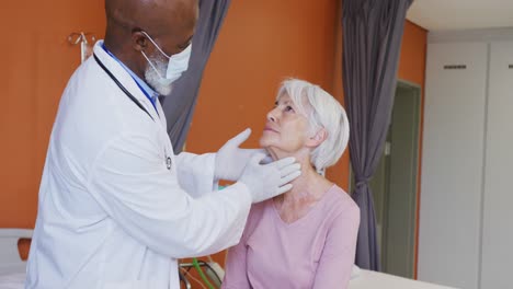 Médico-Varón-Afroamericano-Examinando-El-Cuello-De-Una-Paciente-Caucásica-Mayor-En-El-Hospital