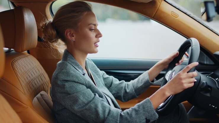 Donna d'affari di profilo che balla in auto. Donna allegra seduta sul sedile anteriore