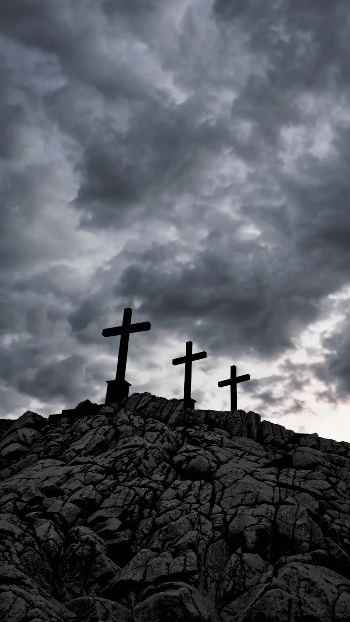 Dramatic video still of three crosses on a rocky hill, captured from a low angle against a stormy