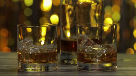 barman pushes, puts glass with golden whiskey, cognac or brandy with ice cubes on wooden table