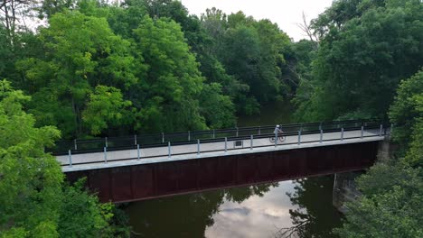 person rides bicycle across bridge over stream