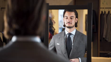 mirror reflection of young bearded man trying on suit in fashion store