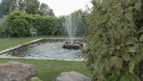 reveal of a beautiful fountain feature on a gorgeously landscaped acreage from behind a hedge on a cloudy and sunny day