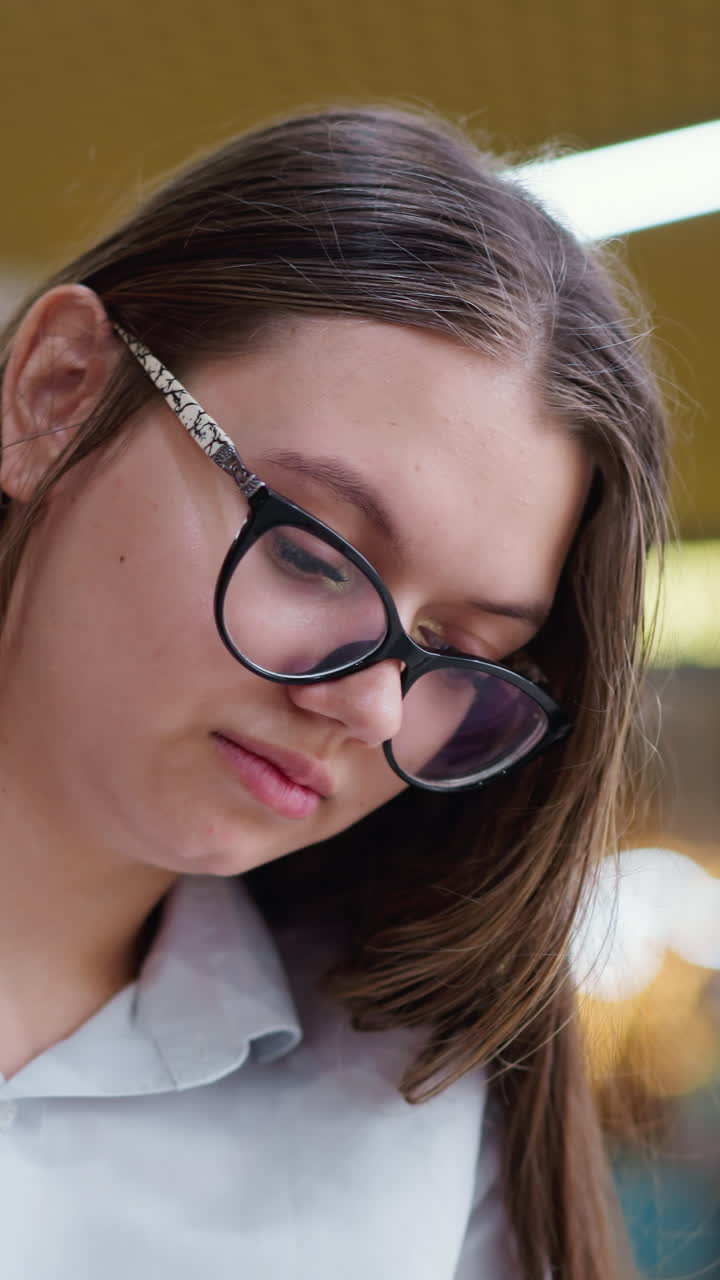 primer plano de una joven pensativa con gafas enfocándose atentamente en el fondo, destacando un momento personal en un entorno ocupado