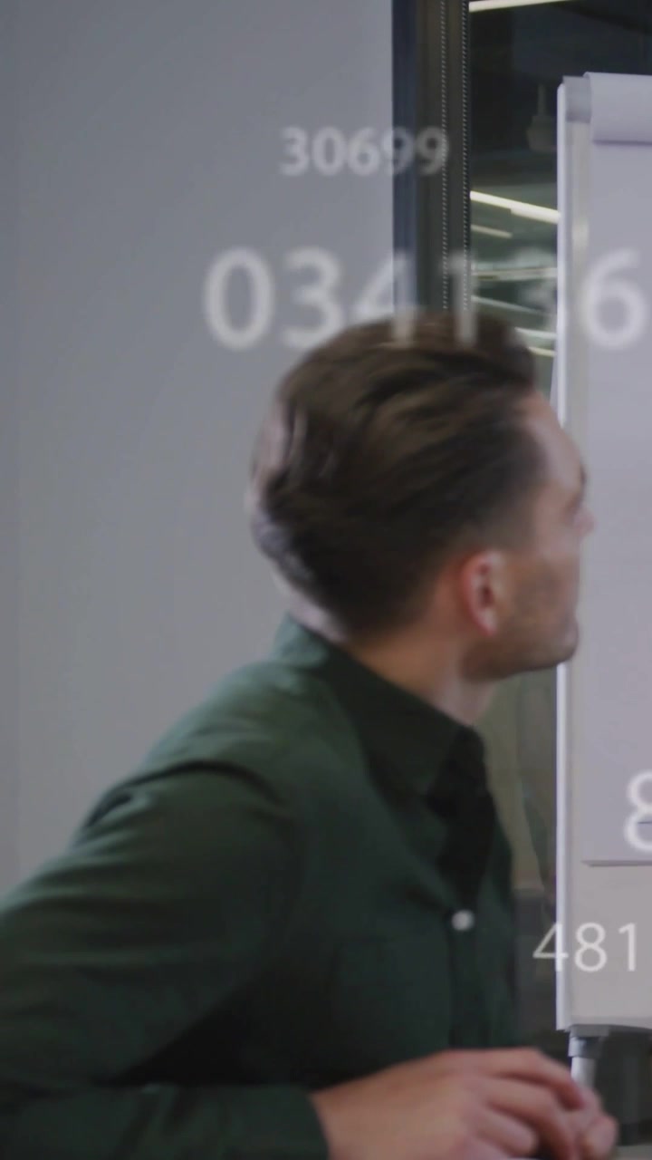 Video verticale: Uomo in ufficio che si gira verso un grafico mentre i numeri scorrono, toccando un pennarello, esaminando.
