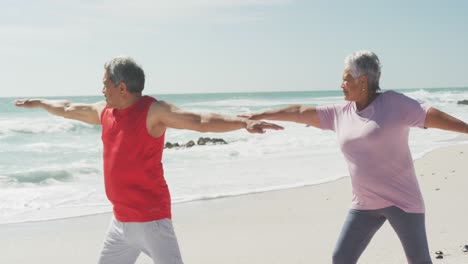 Glückliches-Und-Entspanntes-Hispanisches-Seniorenpaar,-Das-Yoga-Am-Strand-Praktiziert