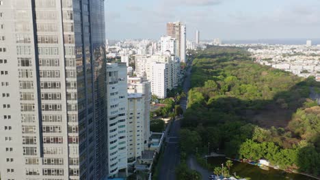 Empty,-desolate-and-deserted-Avenida-Anacaona-shiny-glass-skyscraper-and-downtown-Santo-Domingo-city-skyline-and-view-of-green-tree-park,-covid-19-pandemic,-Dominican-Republic,-overhead-drone-descend