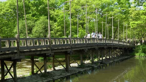 people crossing the old wooden bridge with green trees in background at korean folk village in yongin city, seoul, south korea