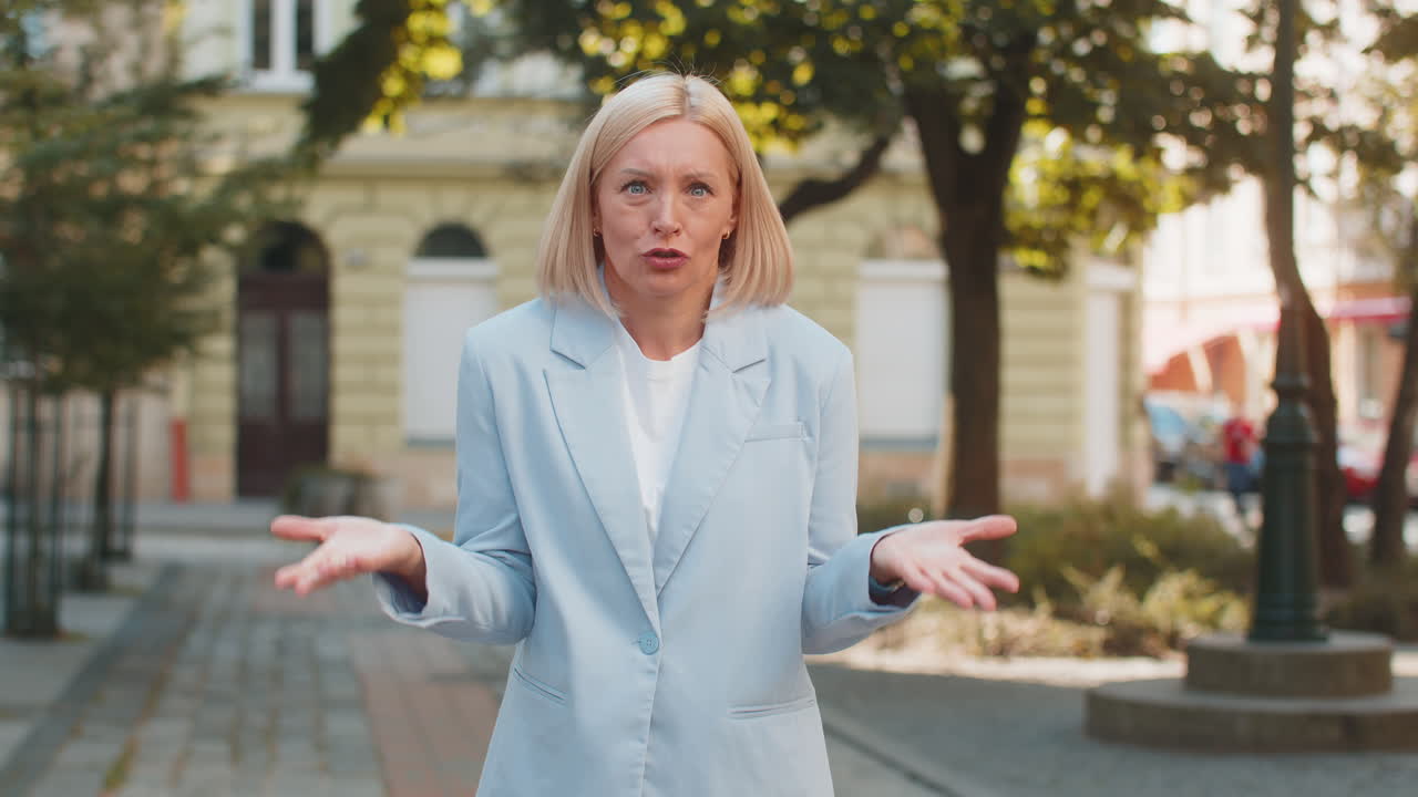 Frustrated mature businesswoman shrugging shoulders dont know answer gesture standing on city street