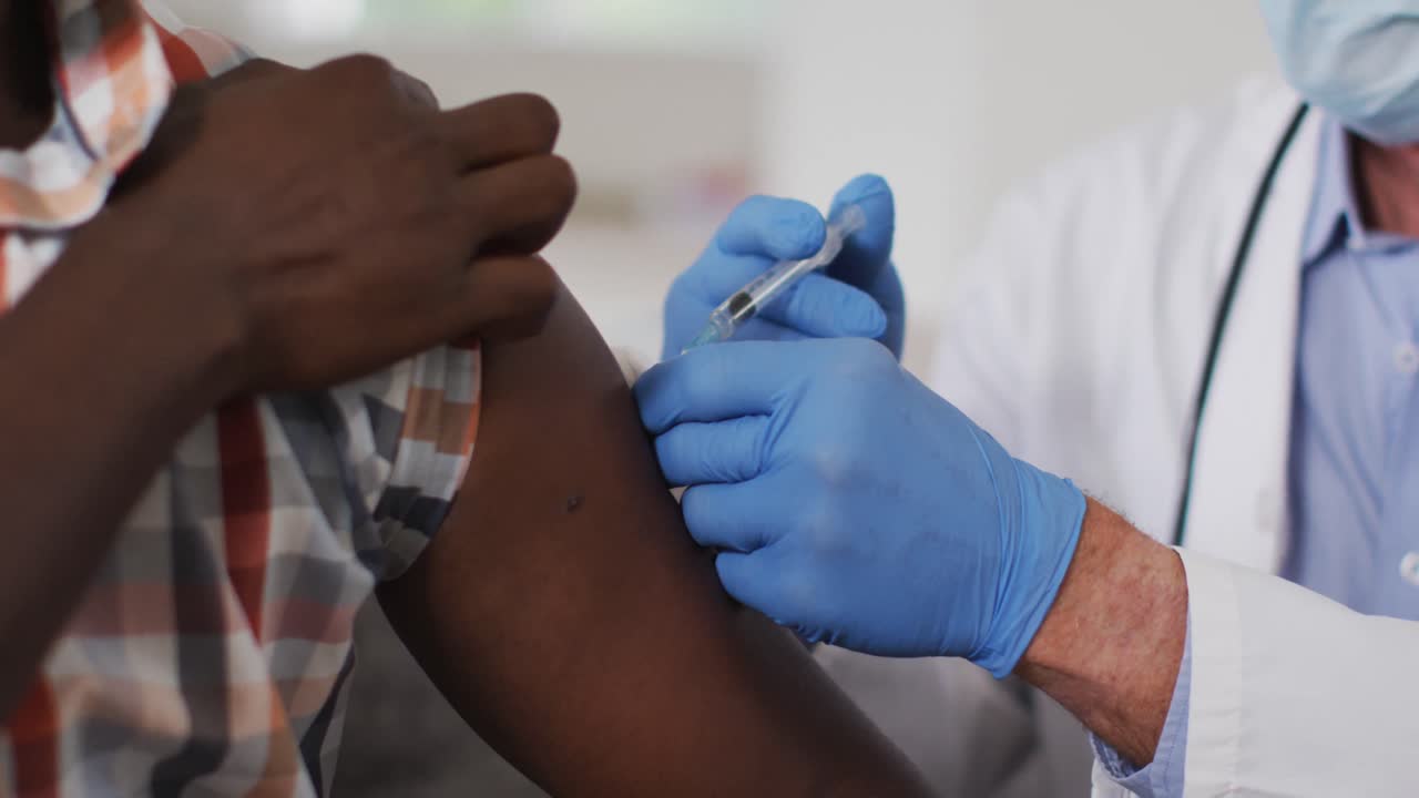 Senior caucasian male doctor vaccinating senior african american man at home both wearing face masks