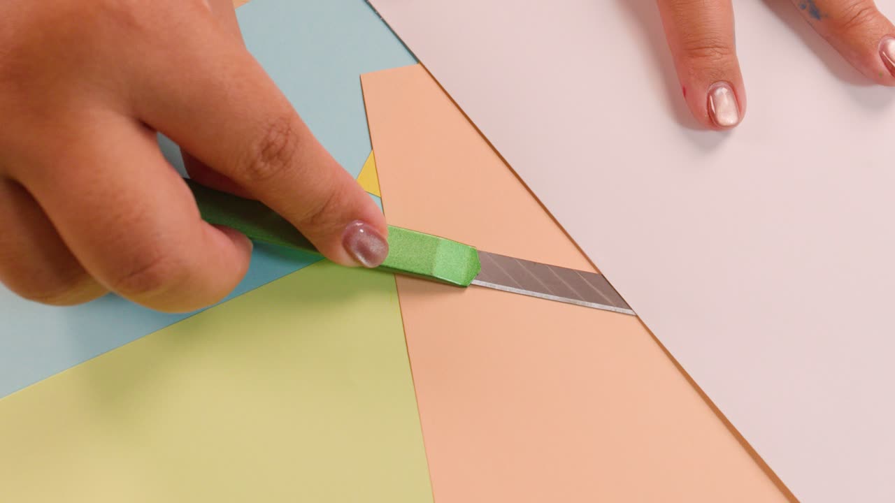 Person uses craft knife to cut and fold colored paper on a well-lit tabletop workspace