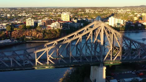 Luftaufnahme-Eines-Drohnenüberflugs-Und-Rundflugs-Um-Die-Story-Bridge,-Wobei-Das-Wahrzeichen-Der-Stadt-Brisbane-Und-Der-Geschäftige-Fahrzeugverkehr,-Der-Den-Fluss-Zwischen-Kangaroo-Point-Und-Fortitude-Valley-Bei-Sonnenuntergang-überquert,-Eingefangen-Werden