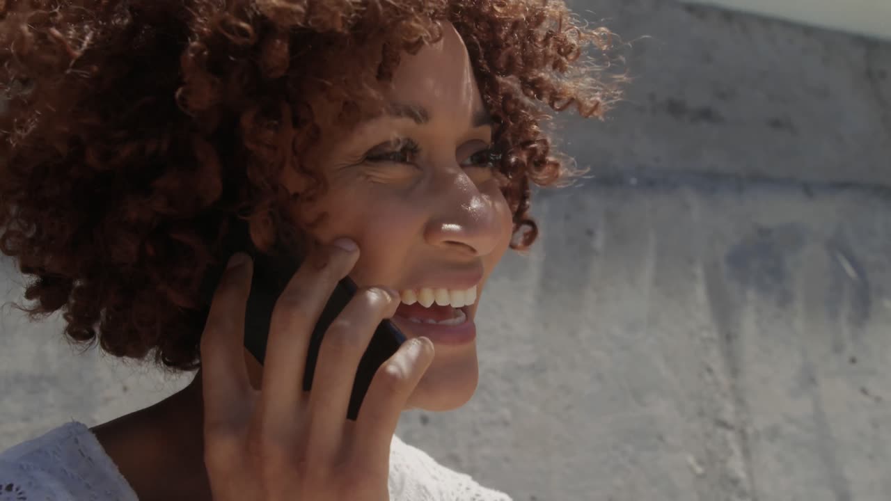 Side view of young African american woman talking on mobile phone at beach in the sunshine 4k