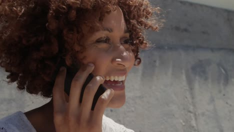 Seitenansicht-Einer-Jungen-Afroamerikanischen-Frau,-Die-Am-Strand-In-Der-Sonne-Mit-Dem-Mobiltelefon-Spricht-4k