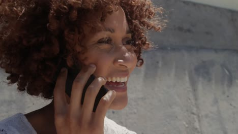 vista lateral de uma jovem mulher afro-americana falando em telefone celular na praia ao sol 4k