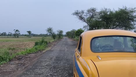 Rückaufnahme-Eines-Gelben-Taxis,-Das-In-Einer-Kaputten-Straße-In-Einem-Indischen-Dorf-In-Bengalen-Feststeckt