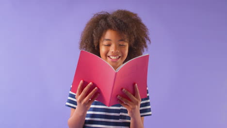 fotografía de estudio de un niño estudiando el libro de ejercicios escolar contra un fondo púrpura