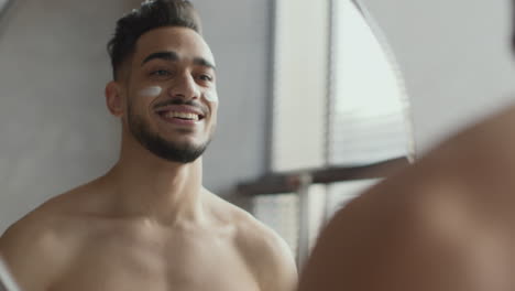 man applying face cream in front of a mirror