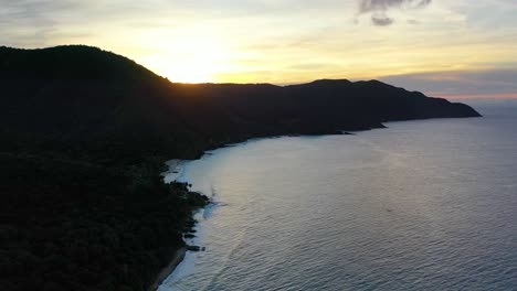 early morning drone shot shows the caribbean sea near st. croix bathed in warm, vibrant light from a colorful sky, illuminating a quiet peninsula and tranquil shoreline below