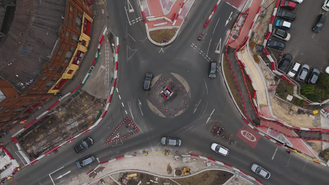 Top down rising circling drone shot of busy roundabout under construction. Safety bollards surround the intersection and cars safely navigate the roads