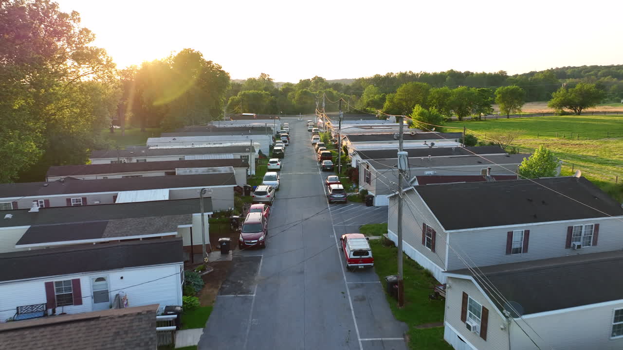 Aerial flight over street in mobile home park. Beautiful sunset shines into lens. Small affordable, run down housing in America