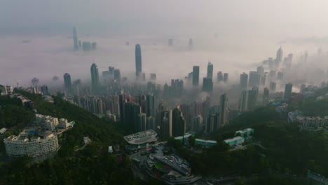 backwards ascending drone shot of hong kong city with skyscraper buildings over fog in the morning