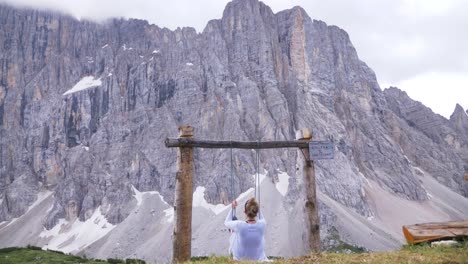 Female-blonde-tourist-on-a-natural-swing-up-in-the-mountains-of-Alleghe-in-the-nature-on-a-sunny-day-in-Italy