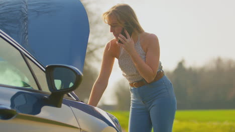 frustrated woman with broken down car on country road calling for help on mobile phone