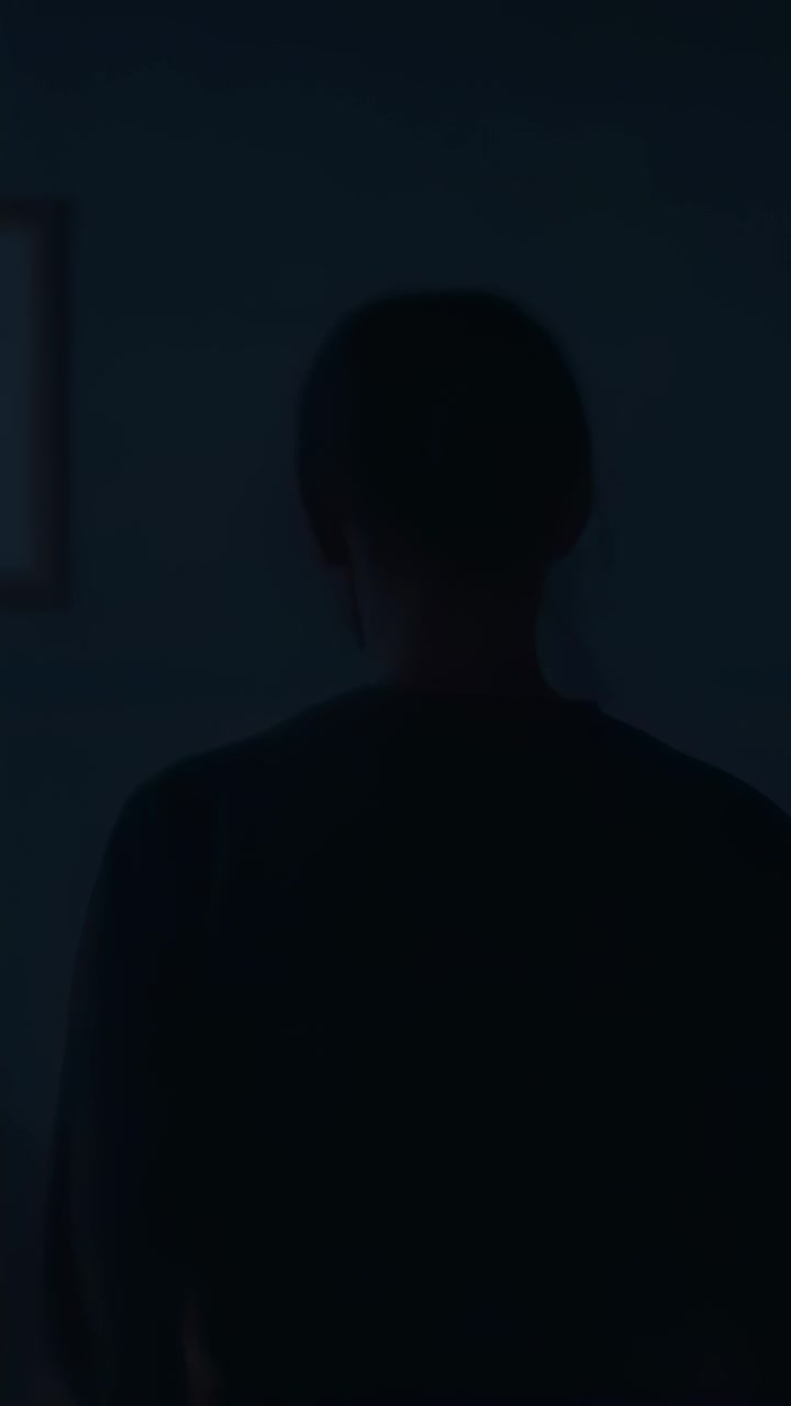 Vídeo vertical: adulto em pé vestindo blusa escura, inclinando a cabeça e virando o pescoço para a direita em casa, quadro na parede