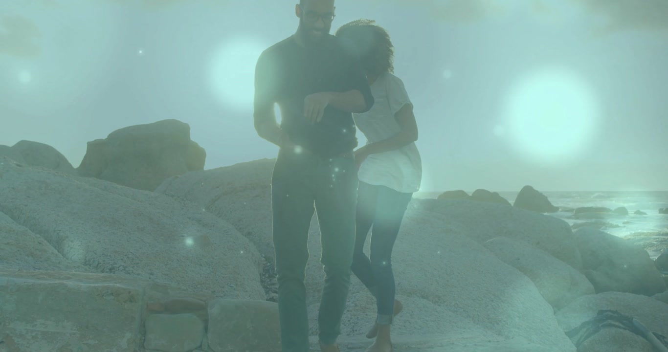Woman reaching to steady on man's arm initiating couple hugging on shore under sunlight for travel