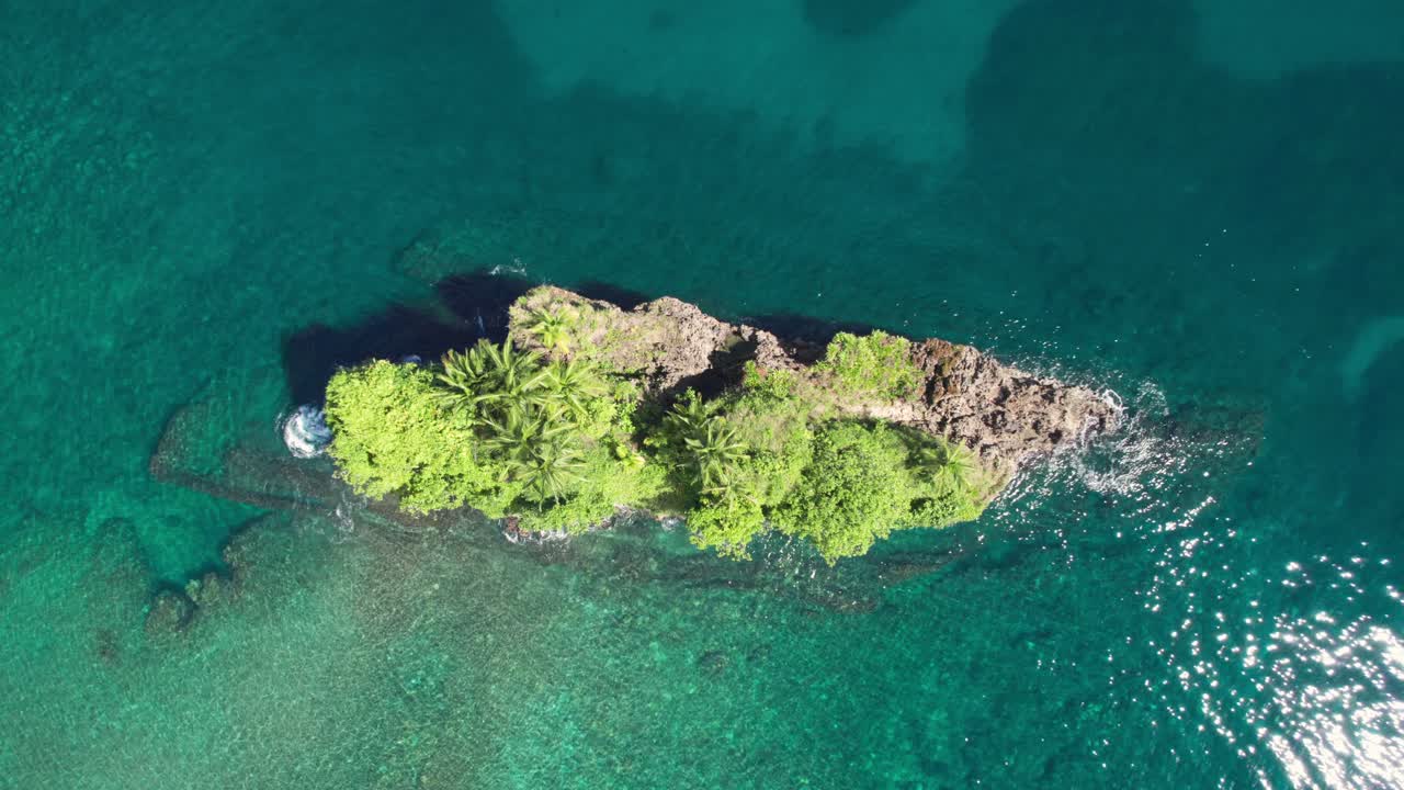 Aerial cenital orbit above Isla Cocles showing the small lush island surrounded by clear turquoise waters on a sunny day.