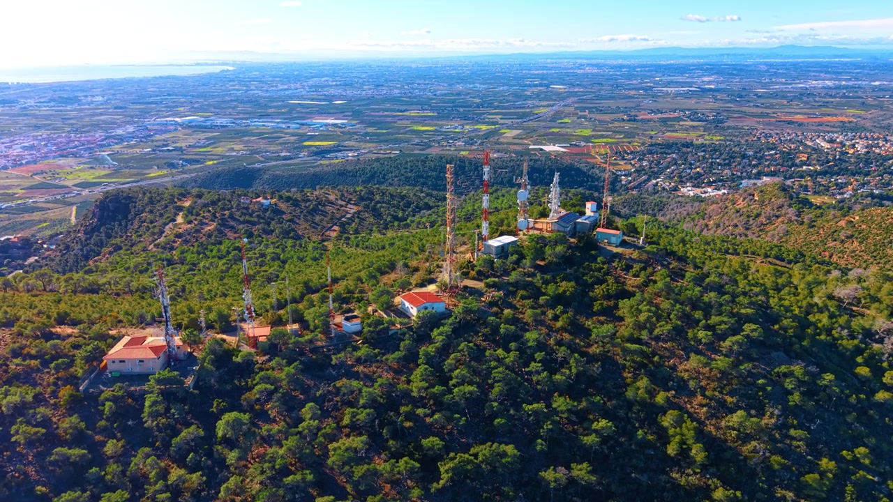 Vista aerea di antenne radio su una collina con pianure costiere. Torri di comunicazione su una cima di montagna che domina un paesaggio costiero pianeggiante e aree urbane