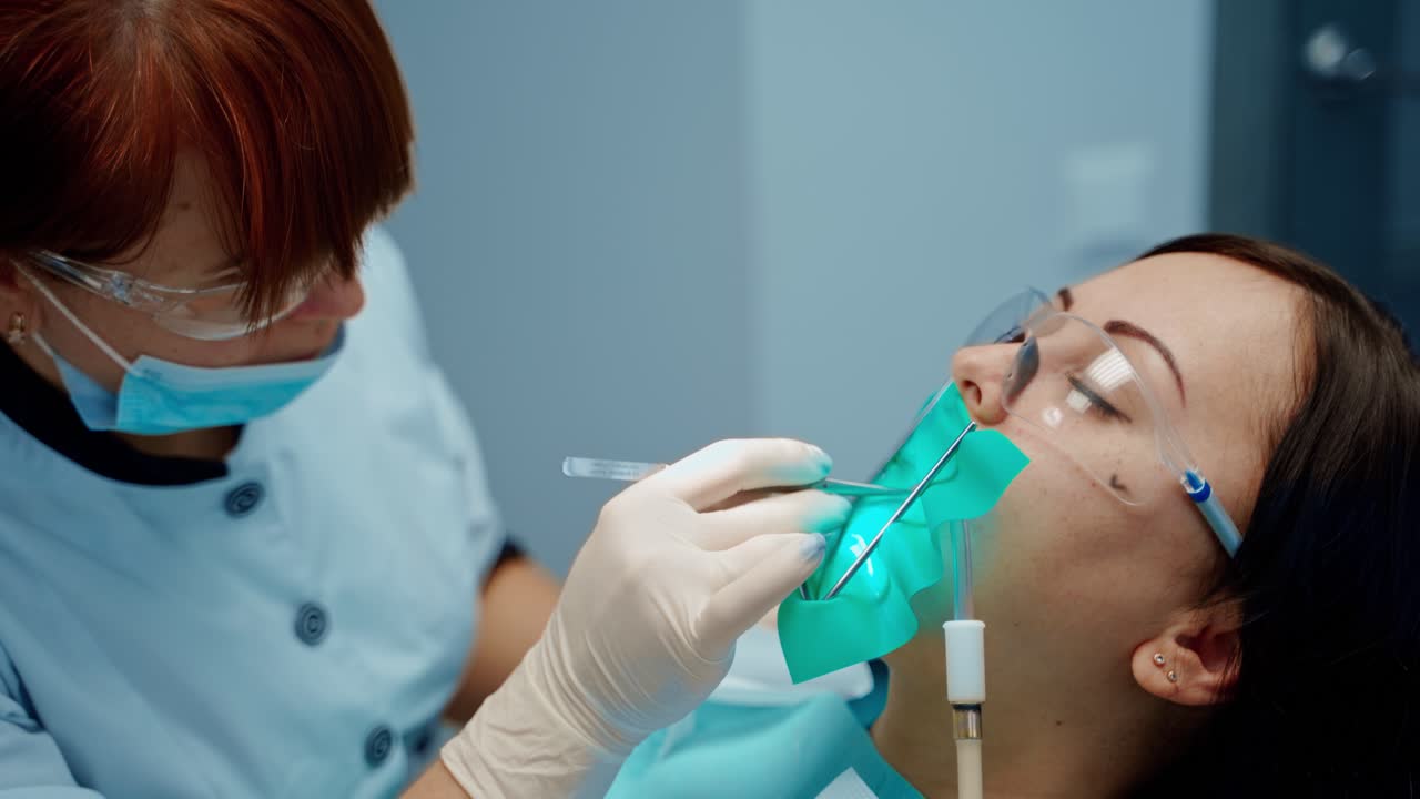 Face of a patient in protective glasses in the dental chair. Professional stomatologist treating woman's teeth in dental center. Stomatology concept.