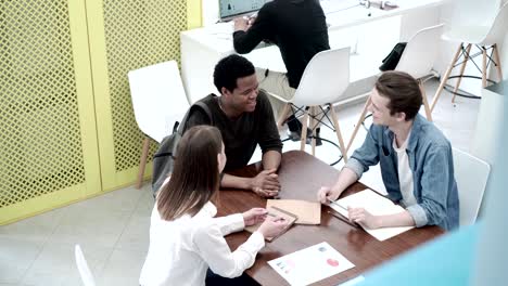 group of three cheerful college students sitting at desk, chatting and discussing homework after classes