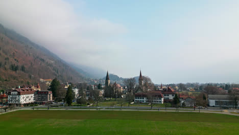 Drone-soars-across-green-open-field-to-chapels-in-Interlaken-Switzerland