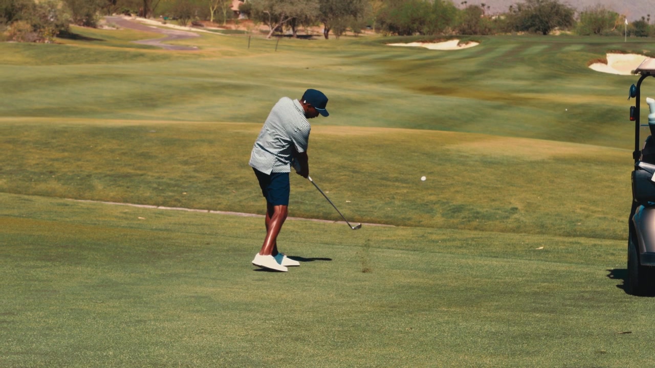 Un golfista esegue un approccio netto con il ferro dal fairway, accanto a un golf cart su un campo da golf nel deserto, al rallentatore, adatto per montaggi di consigli sul golf e promozioni di campi.