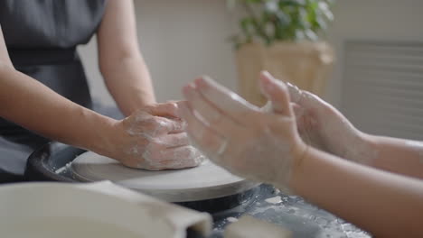 a female potter's wheel sculpting teacher explains how to work and teaches an elderly woman to work with clay and make mugs and jugs. master class for pensioners. pottery courses