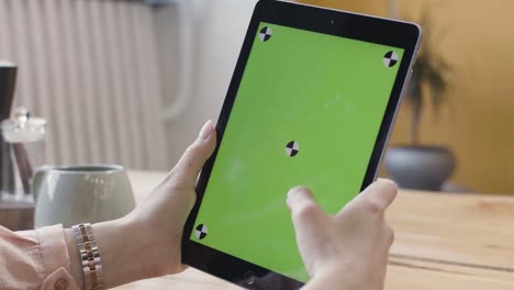 woman using a tablet with a green screen in a cafe