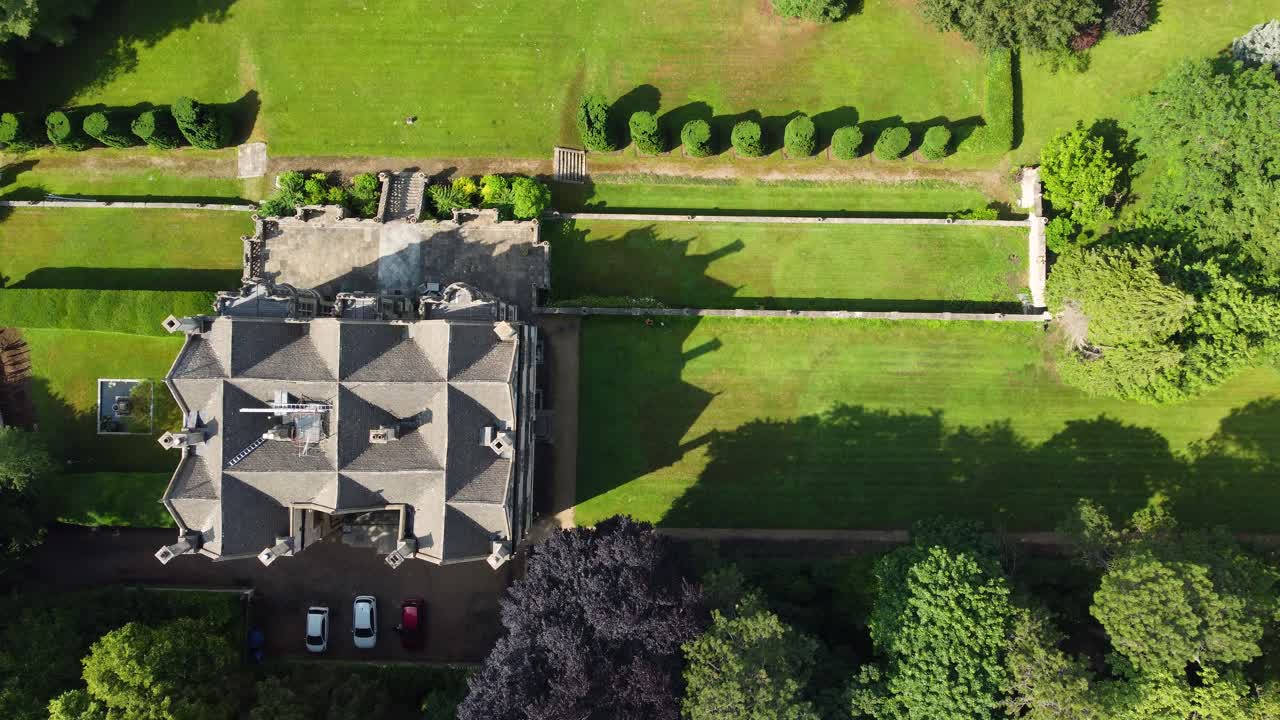 Drone descends in a vertical top-down shot above a large historic house, revealing the symmetrical garden layout and surrounding trees