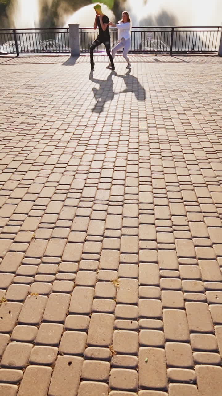 Modern dancers are dancing in the street. Urban lifestyle. Hip-hop generation. Boy's and girl's emotional moves on the video. Paving stones and young dacing couple at fontain background. Aerial view. Young beauty dances behind handsome boy. Vertical video