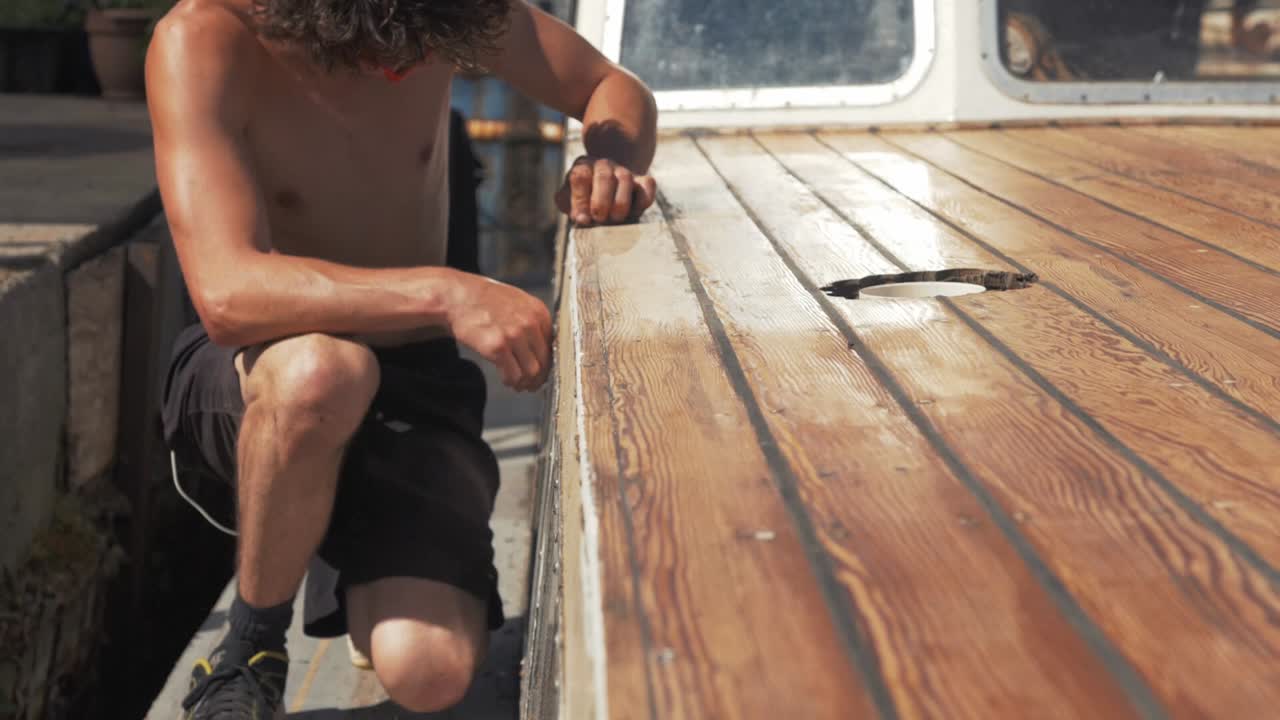 Junger Mann schleift Holz auf einem Holzboot von Hand