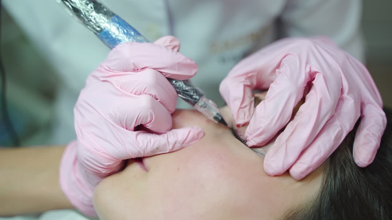 a beautician in gloves is making a permanent makeup of eye for a woman with the using of a professional needle. Modern cosmetology methods