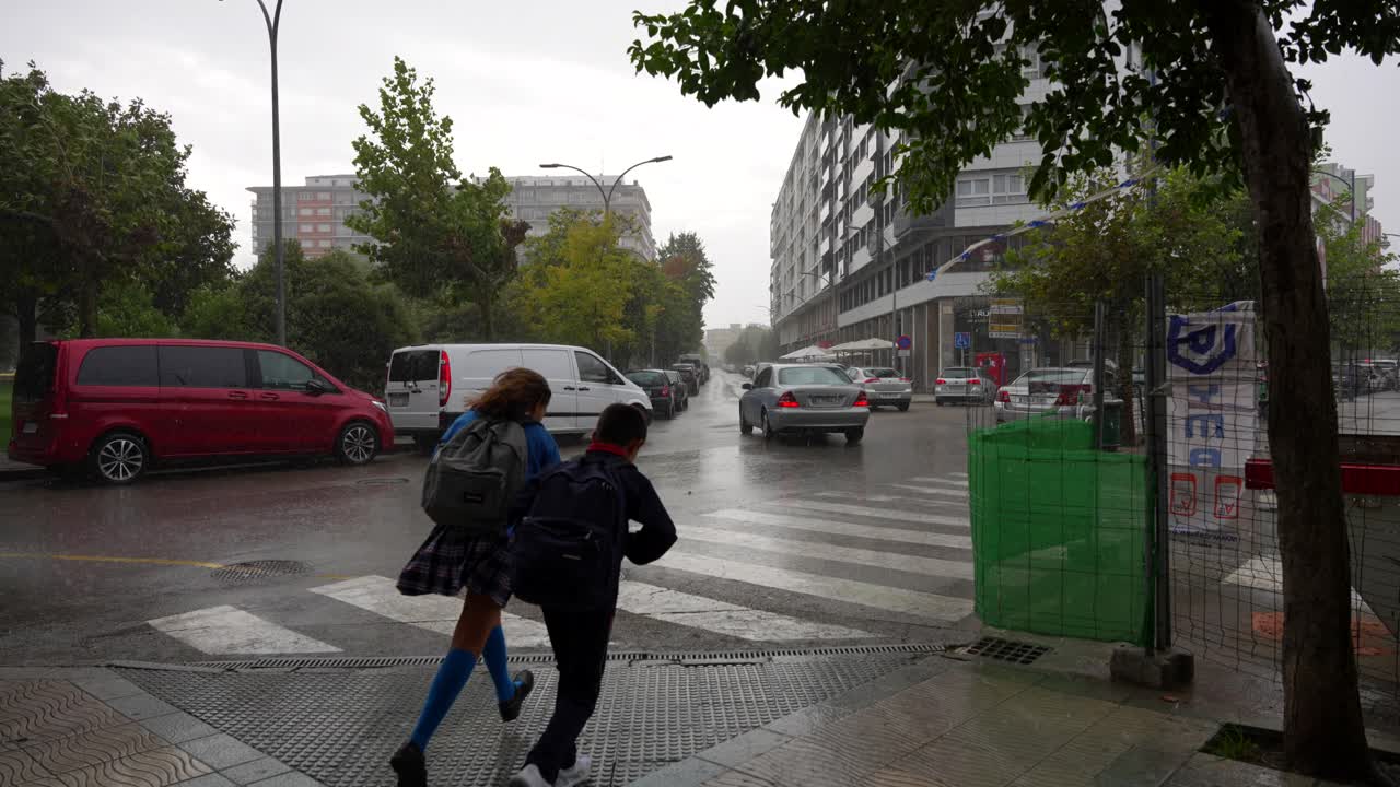 Children dash across a rainy crosswalk in Laredo, Cantabria as cars line the wet city street