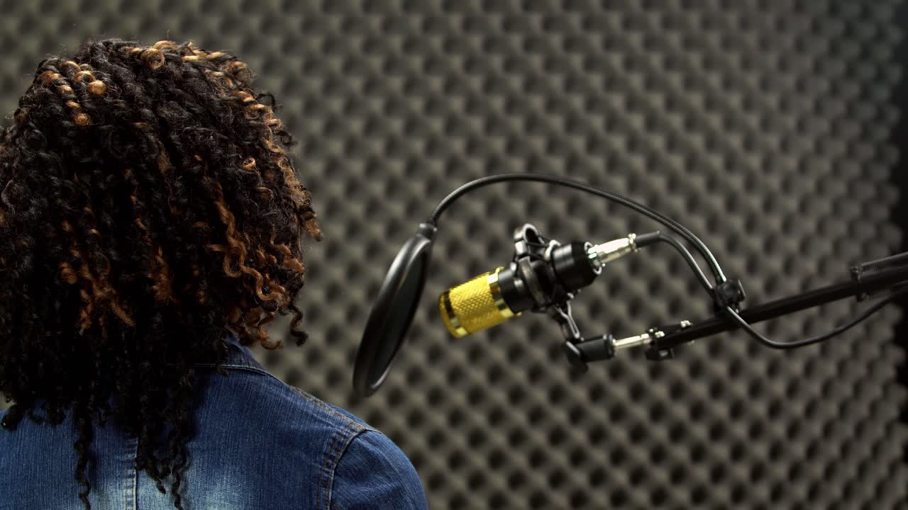 mujer negra afroamericana de cabello alfro canta una canción en voz alta y expresa sentimientos con un sonido potente sobre un condensador de micrófono colgante