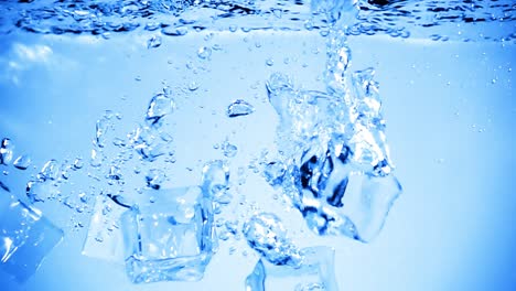 cubos de hielo caídos en el agua con burbujas de aire.